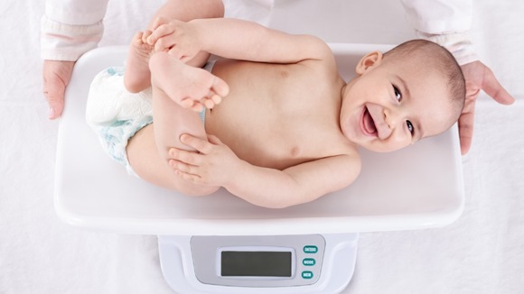 lachende baby wordt op weegschaal gewogen